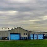 Steel farm building surrounded by green fields of grass during dust.